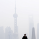 A woman wearing a face mask stands on a bridge in front of the financial district of Pudong amid heavy smog in Shanghai, China, December 15, 2015.